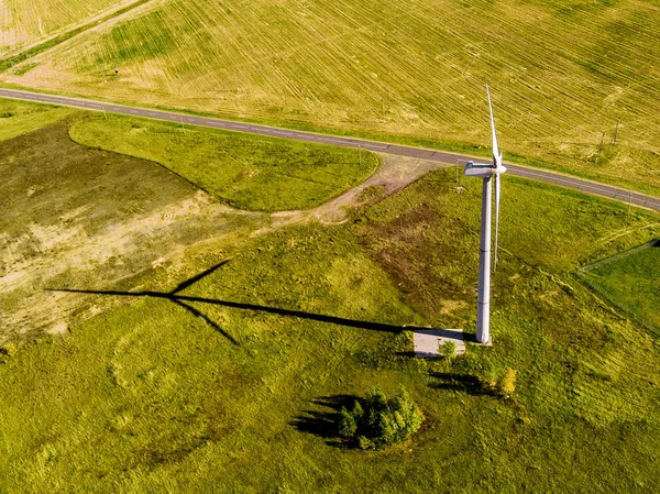 Vista dall'alto di enorme campo verde brillante e solitaria turbina eolica bianca che getta ombra parallela alla strada — Foto Stock