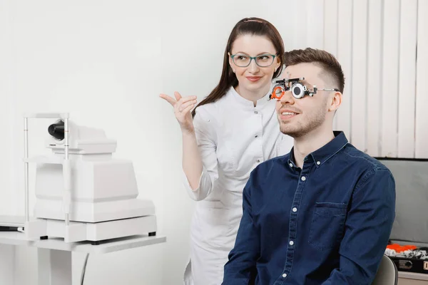 Ο άνθρωπος κάθεται και χαμόγελα στο σιδερένιο σκελετό για επιλογή γυαλιά φακούς στα μάτια υποδοχή Οφθαλμίατρος. — Φωτογραφία Αρχείου