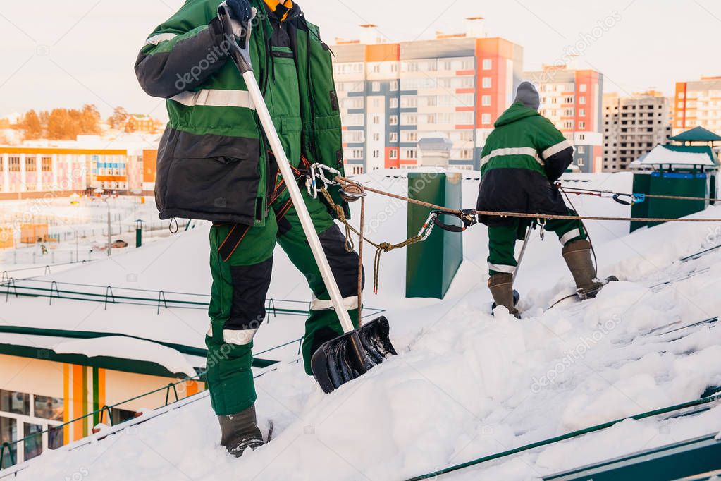 Team of male workers clean roof of building from snow with shovels