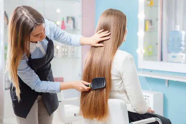 Master hairdresser woman combing hair of client in chair beauty salon spa