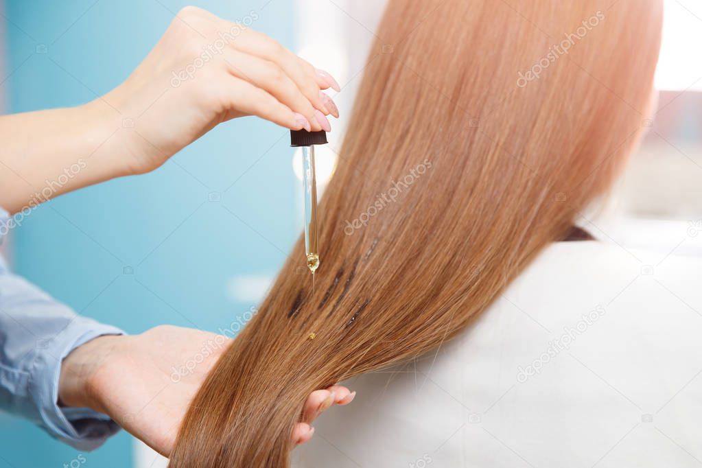 Master hairdresser applies oil to hair care for and restore growth of cuticles woman.