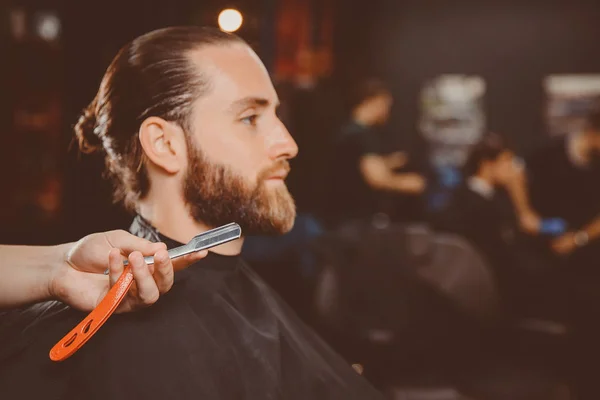 理发师手中的特写剃须刀 背景客户正在等待剃须的胡子和胡子 — 图库照片