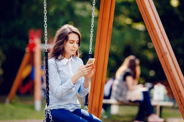 Girl student teenager swinging on a swing and using phone for communication looks in frame.