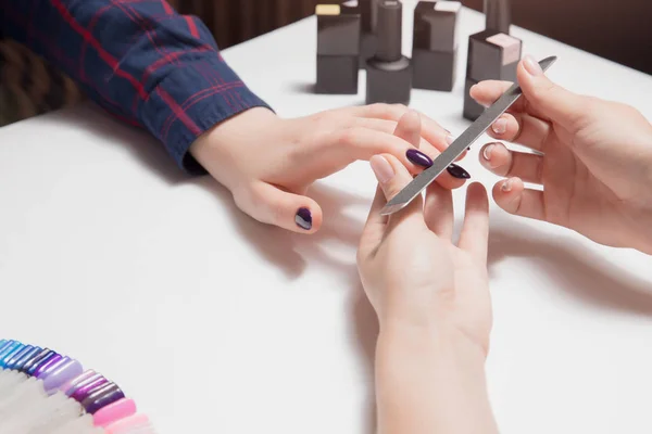 Manos bien arregladas de manicura lima uñas púrpura de cerca. Barnices de gel en el fondo . —  Fotos de Stock