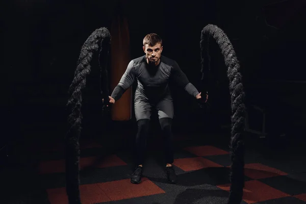 Men with battle rope in functional training fitness gym. Concept workout. Black background