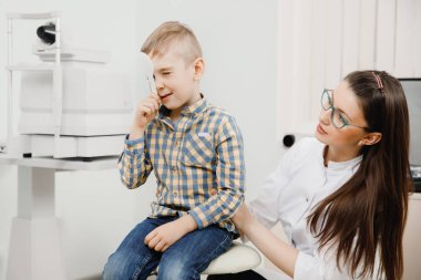 Küçük sarışın çocuk kareli gömlek göz göze ait spatula ile vizyon ofisinde bir genç kadın doktor kontrol etmek için kapalı.