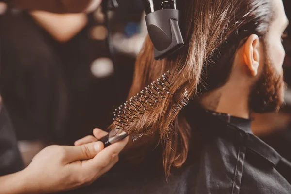 Barber makes hair styling to man with hairdryer and comb.