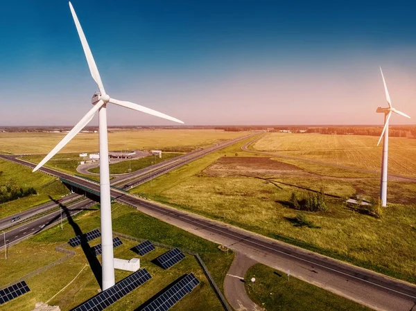 two parallel wind stations cast shadow green grass and highway bright Sunny day