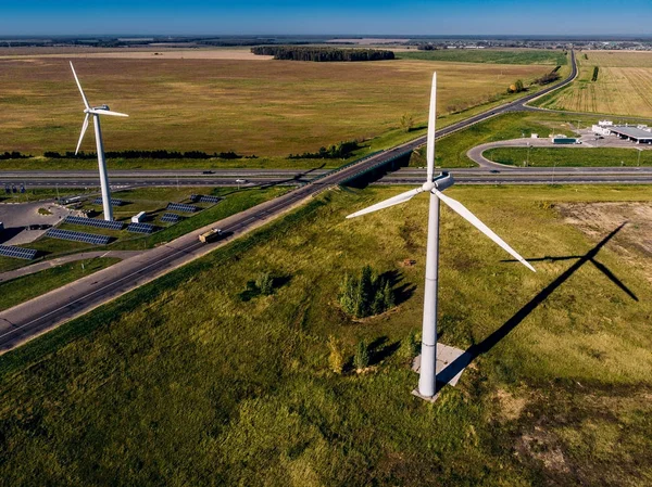 Piccoli camion cavalca su grande strada e enormi turbine eoliche sfondo cielo blu chiaro, generando elettricità lungo — Foto Stock