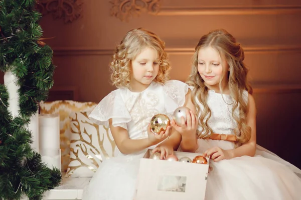 姐妹们, 穿着白色礼服的小女孩在树的背景下交换圣诞礼物 — 图库照片