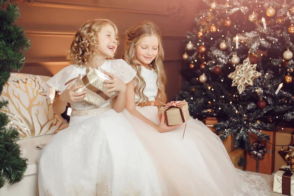 Irmãs meninas em vestidos brancos trocam presentes de Natal no fundo da árvore — Fotografia de Stock