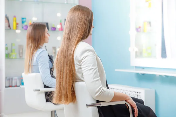 Dos chicas con el pelo largo y grueso bien arreglado sentarse silla en el salón de belleza, esperando —  Fotos de Stock