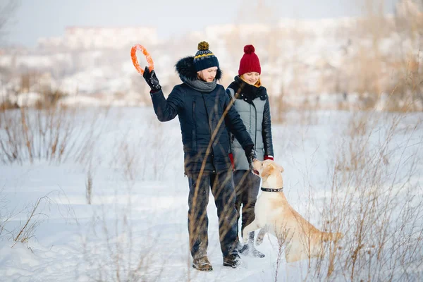 Uomo e giovane donna lanciano giocattoli per cani labrador nella neve in inverno . — Foto Stock