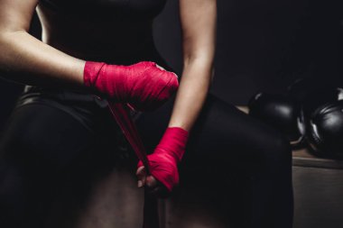 Kız siyah arka plan üzerine üniformalı zorlu mücadele için hazırlanıyor, kırmızı ve pembe, boks eldiveni yanında yalan spor koruyucu sargılar ellerini sarar