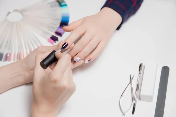 Hermosas manos mujer manicura cepillo de sujeción para gel esmalte y aplicar recubrimiento en las uñas del cliente en camisa púrpura . —  Fotos de Stock