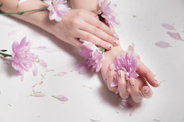 Cilt Bakımı. Şık fotoğraf. Çıplak manikür. Güzel erkek holding pembe çiçekler eller. Yaprakları üzerinde dağınık