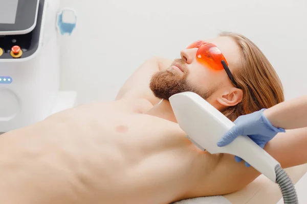L'uomo barbuto bello è venuto a procedura di depilazione laser. Medico tratta la sua ascella con un apparato speciale — Foto Stock