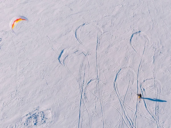 Snowkiting. Male athlete on mountain skiing with dreams kite free ride on frozen lake. Aerial view — Stock Photo, Image