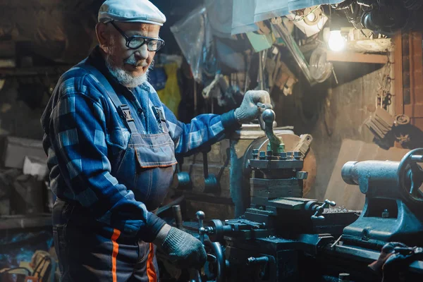 El tornero adulto mayor maneja el metal en la máquina. Concepto trabajador de pensiones industrial, lugar de trabajo — Foto de Stock