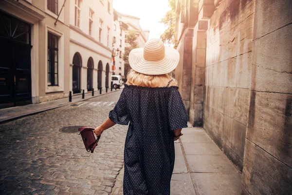 Молодая женщина ходит с сумкой и в соломенной шляпе туристических улиц солнечные лучи на открытом воздухе старого города — стоковое фото