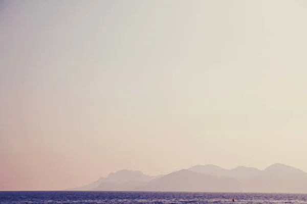 Havet solnedgång. Vanilla Sky, vatten mot berg på avstånd. Koncept avslappning och semester — Stockfoto