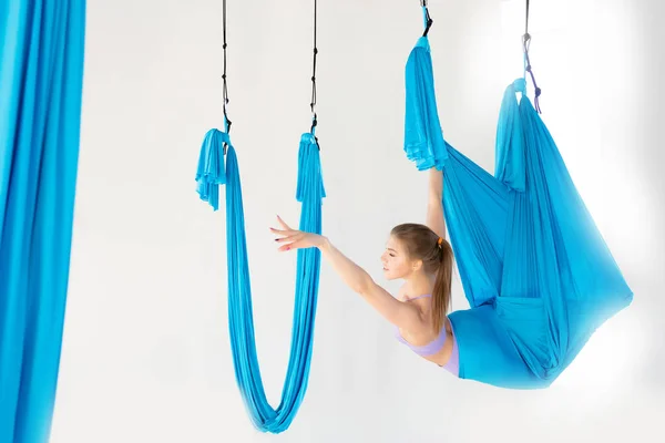 Aero fly yoga vacker kvinna i uniform Trainer visar asana stretching på blå hängmatta i vit klass — Stockfoto