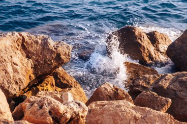 Dalgalar ve sıçramaları ile Fırtınalı deniz keskin taşlar, sıcak gün, güneş ışığı tatili