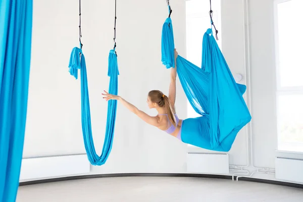 Vacker ung kvinna leende på att öva Aero fly yoga i vit Studio på blå hängmattor. Koncept stretching meditation, — Stockfoto