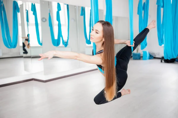 Young beautiful women gymnast in blue hammock. Aerial fly yoga in white studio