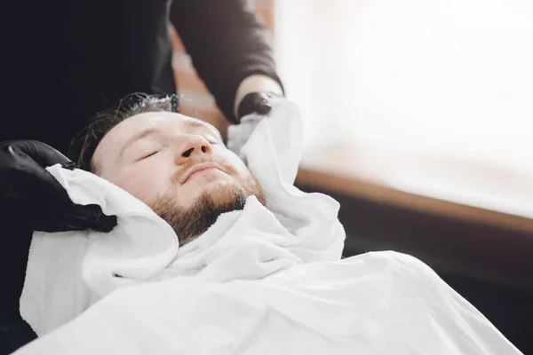 Barber steam face skin of man with hot towel before royal shave in Barbershop