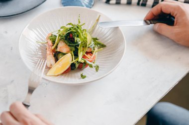 Karides, arugula, limon, domates derin kase, erkek elleri ile salata, çatal çatal tutar. Açık arka plan. Üstte görüntü
