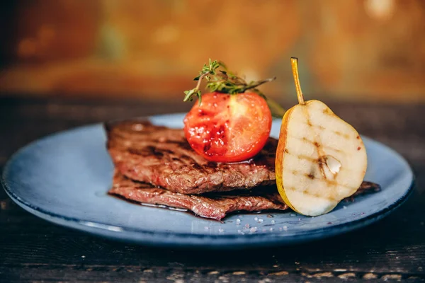 Restaurant cooking, beautiful serving of dishes, grilled meat steak is decorated with pear and tomato. Black background