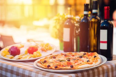 Domatesli İtalyan pizzası, mozzarella peyniri, fesleğen, siyah zeytin. Arka planda, şarap ve gün batımında ışık vurgulamak