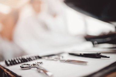 Kuaför için araçlar: makas, tarak ön planda, müşteri sandalye arka planda oturur