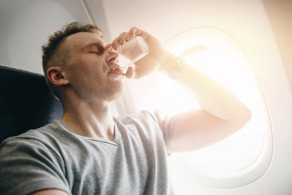 El hombre bebe agua en un avión antes de despegar. Concepto pone oídos — Foto de Stock