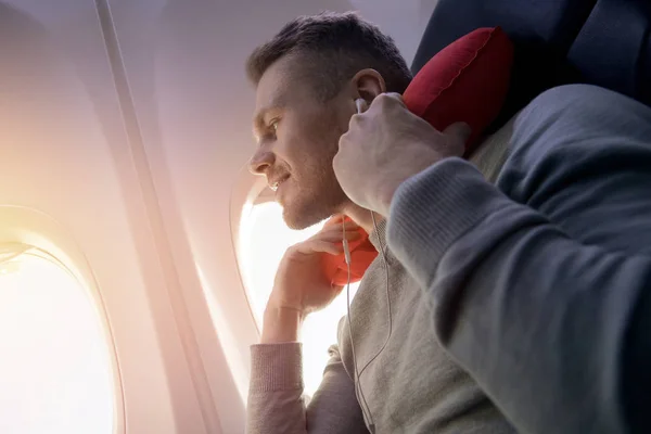 Pasajero masculino de avión escucha música y disfruta de almohada para dormir en silla . — Foto de Stock