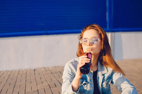 Москва, Россия - 27 июня 2019 года: Красивая молодая женщина счастливо пьет кока-колу стеклянную бутылку соды в руке, закат — стоковое фото