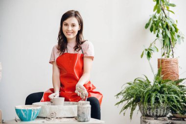 Avrupalı sanatçı kız çömlekçi tekerlek üzerinde kil yemekleri yapma, mutlu ve gülümseyerek. İş için aşk kavramı, zanaat