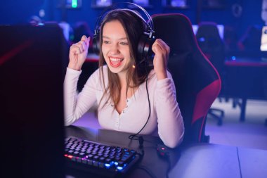 Flamalı güzel kız profesyonel oyuncu kulaklıklı, kırmızı ve mavi renkli online oyun bilgisayarı oynuyor.
