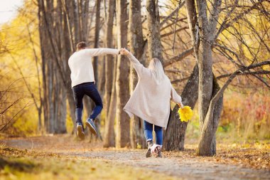 Aşık çift sonbahar parkında kızın elinde akçaağaç yapraklarıyla yürür, adam mutluluktan atlar. İlk aşk konsepti