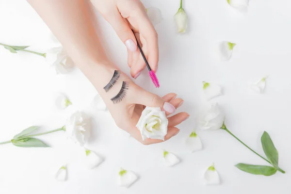 Hände Mädchen Meister Wimpernverlängerung auf weißen Blumen Hintergrund mit rosa Pinsel, Ansicht von oben. Schönheitskonzept — Stockfoto