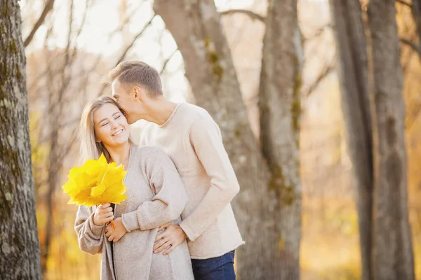 Loving couple in autumn park with maple leaves, man whispers to beautiful girl ear declaration of love — Stock Photo, Image