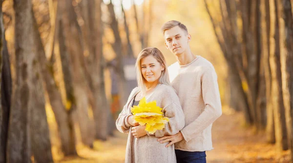 Couple aimant dans le parc d'automne avec des feuilles d'érable dans les mains de la fille, lumières vives — Photo