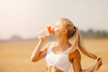 Güzel sarışın spor şişesinden parkta yoga yaptıktan sonra su içiyor.