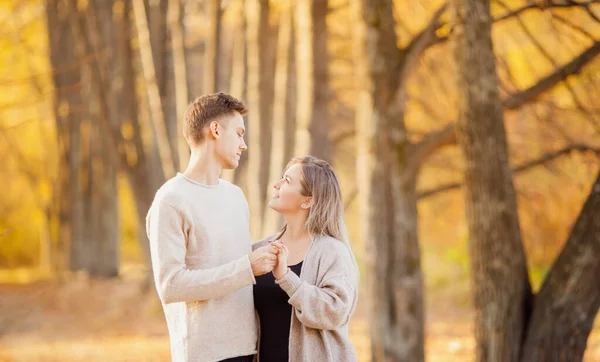 Liebendes Paar steht umarmt im Herbstwald in hellbeigen Pullovern, gelbem Hintergrund mit Blättern — Stockfoto