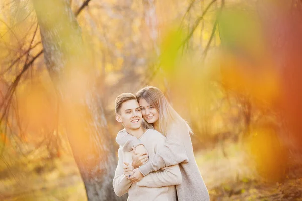 Loving couple in autumn park with maple leaves, girl whispers to beautiful man ear declaration of love — Stock Photo, Image