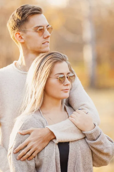 Любящая пара в солнечных очках круглой формы обнимает свитер на фоне осеннего парка — стоковое фото