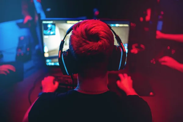Профессиональный геймер, играющий в онлайн игры турниры ПК компьютер с наушниками, размытый красный и синий фон — стоковое фото