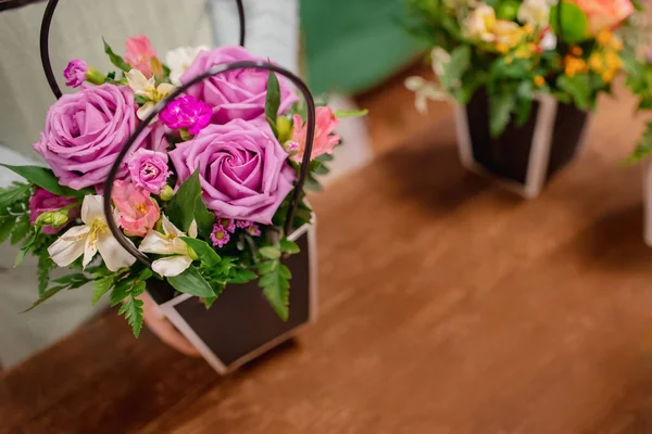 Florist girl with her hands makes bouquet flowers composition of pink roses, fern in gift box. Top view on workplace