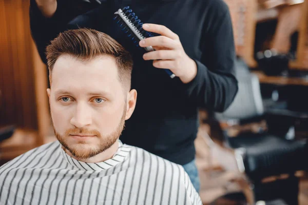 Close-up master Barber does hairstyle and styling with dryer hair to guy. Concept Barbershop — Stock Photo, Image